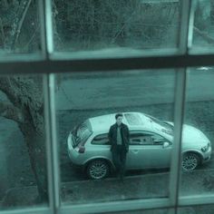 a man standing next to a parked car in front of a window on a rainy day