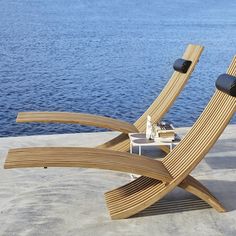 two wooden lounge chairs sitting on top of a sandy beach