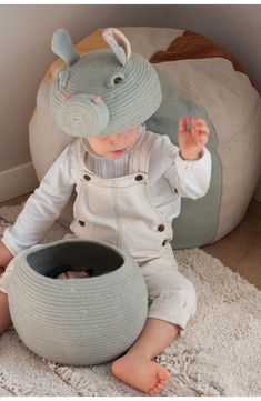 a small child sitting on the floor next to a large pot and wearing a hat