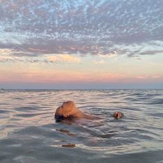 a person floating in the water with their head above the water's surface as the sun sets