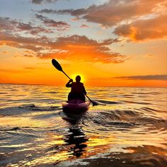 a person in a kayak paddling on the water at sunset