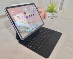 an open laptop computer sitting on top of a white rug next to a potted plant