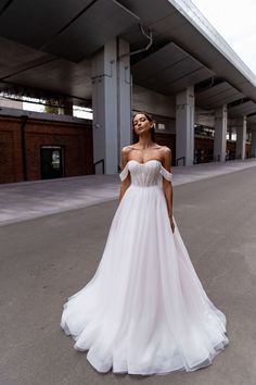 a woman in a white wedding dress is standing on the street with her hands behind her back