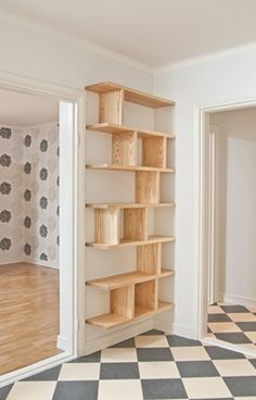 an empty room with wooden shelves on the wall and checkered flooring in front of it