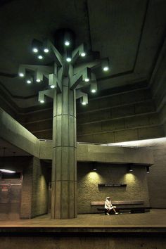 a person sitting on a bench in front of a tall building with lights hanging from the ceiling