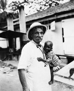 an old black and white photo of a man holding a baby in his arms while wearing a hat