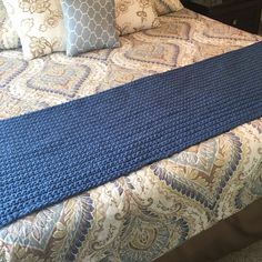 a blue crocheted blanket is on top of a bed with pillows and blankets