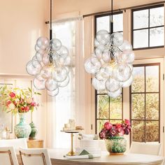 two chandeliers hanging from the ceiling above a dining room table with white chairs