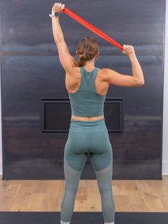 a woman in tights holding a red object up to her head while standing on a yoga mat