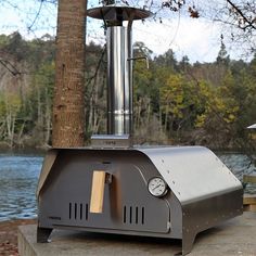 an outdoor bbq grill sitting next to a body of water with trees in the background