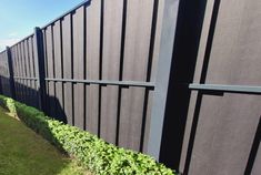 the side of a fence with green plants growing on it and grass in front of it