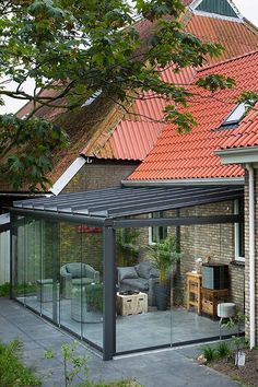 a glass enclosed patio area in front of a house with red tiled roof and brick walls