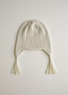 a white knitted hat with tassels on the top and bottom, against a white background