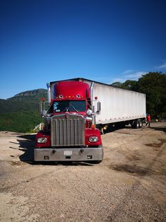 a red semi truck parked on top of a dirt road