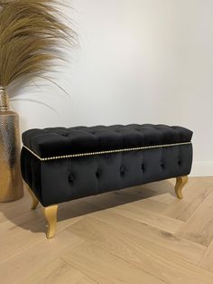 a black bench sitting on top of a wooden floor next to a vase with grass in it