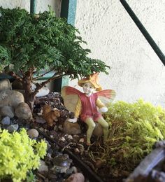 a fairy figurine sitting on top of a pile of rocks next to a tree