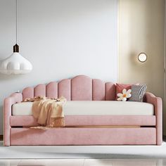 a pink daybed with pillows and blankets on it in front of a white wall