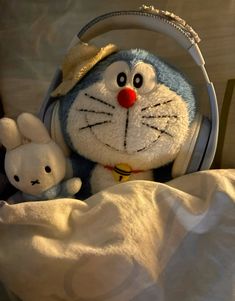 a stuffed animal with headphones on sitting next to a stuffed rabbit in the bed