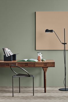 a desk with a lamp and books on it in front of a green painted wall