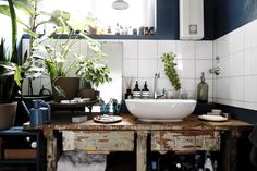 a bathroom sink sitting under a window next to a wooden table with bottles on it