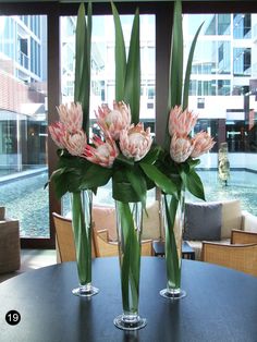 two vases filled with flowers sitting on top of a black table next to a window