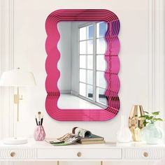 a pink mirror sitting on top of a white table next to a lamp and vase