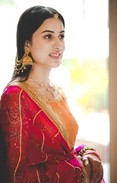 a woman in a red and gold sari is smiling at the camera with her hand on her hip