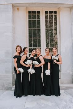 a group of women standing next to each other in front of a building holding bouquets