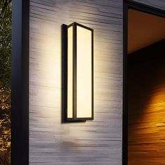 a modern outdoor wall light on the side of a white building with wood paneling