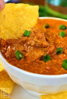 a hand dipping a tortilla chip into a bowl of chili