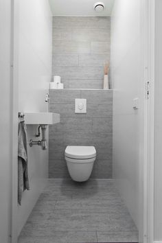 a white toilet sitting inside of a bathroom next to a sink under a light fixture