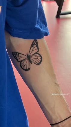 a person with a butterfly tattoo on their left arm and wrist, standing in front of a pink floor