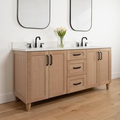 two mirrors on the wall above double sinks in a bathroom with wood floors and white walls