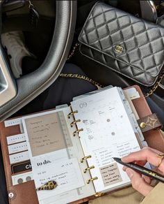 a person holding a pen and writing in a planner book next to a car steering wheel