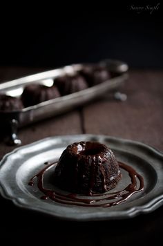 a chocolate cake on a plate with sauce drizzled over it and two spoons in the background