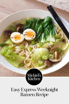 a white bowl filled with noodles and vegetables next to chopsticks on top of a wooden table