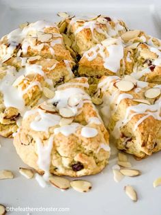 a white plate topped with scones covered in icing and almonds next to sliced almonds