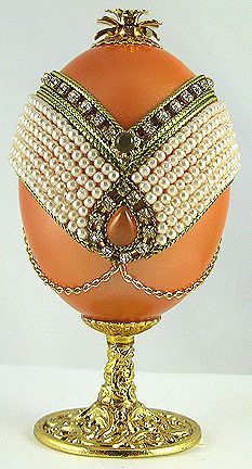 an egg decorated with pearls and jewels on a gold plated stand against a white background