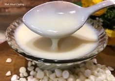 a spoon full of milk sitting on top of a bowl filled with white beans next to yellow flowers