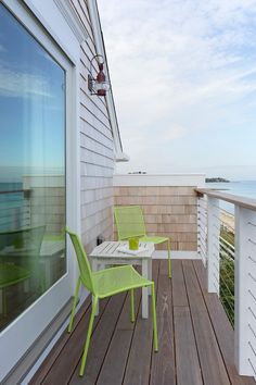 two green chairs sitting on top of a wooden deck next to an open window with the ocean in the background