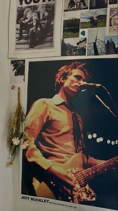 a man playing guitar in front of a wall with pictures on it