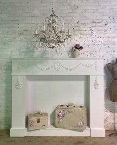 a white fireplace with two suitcases and a chandelier