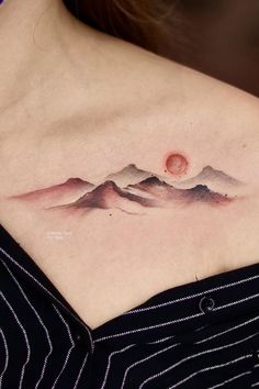 a woman's chest with a mountain scene tattoo on her left side ribcage