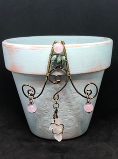 a white pot with some pink beads on it and a wire hanging from the top