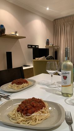 the table is set with two plates of spaghetti and a bottle of wine on it