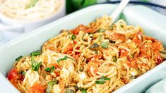 a bowl filled with noodles and vegetables on top of a blue cloth next to a white plate