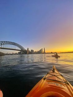 two kayakers are in the water with a bridge in the background at sunset