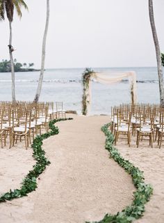 an outdoor wedding setup on the beach with palm trees and chairs lined up along the aisle