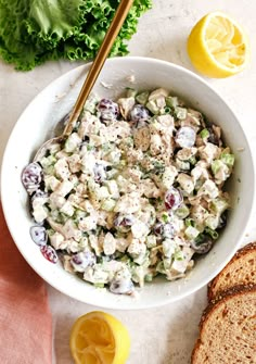 a white bowl filled with chicken salad next to sliced lemons and bread on a table