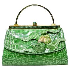 Elegance and glamor right this way! This is a highly designed handbag by none other than Judith Leiber that will be sure to catch people's attention from across the room. This is a BEAUTIFUL Judith Leiber in genuine green alligator in excellent condition. The exterior of this bag has a stunning alligator skin complimented with a unique metal brooch detailing and a gold metal top handle and push lock embellished with green crystals. This handbag is vintage from the early 21st century and is in pr Laura Bush, Mary Frances Handbags, Judith Leiber Handbags, Judith Leiber Bags, Gold Chanel, Unique Handbag, Unique Purses, Judith Leiber, Luxury Purses